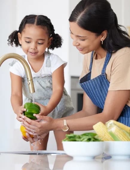 A parent and child washing fresh produce together at the kitchen faucet